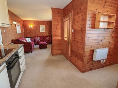 A living area with wooden walls red sofas a kitchen counter an oven and a wooden door at Creag Mhor Lodge Back of Keppoch near Arisaig