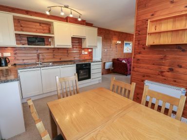 A kitchen and dining area with wooden chairs and table white cabinets and wood panel walls at Creag Mhor Lodge Back of Keppoch near Arisaig