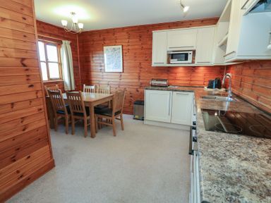 A kitchen and dining area with wooden walls a dining table with six chairs white cabinets and kitchen appliances at Creag Mhor Lodge Back of Keppoch near Arisaig