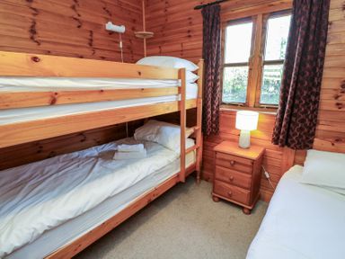 A bedroom with wooden bunk beds a single bed a wooden nightstand with a lamp and a window with curtains at Creag Mhor Lodge Back of Keppoch near Arisaig