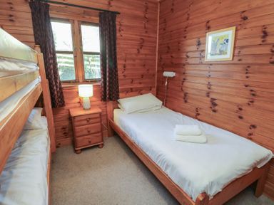 A bedroom with wooden bunk beds a single bed a wooden nightstand with lamp and a framed picture on the wall at Creag Mhor Lodge Back of Keppoch near Arisaig