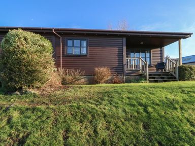 A wooden lodge with windows and a small porch with stairs surrounded by grass and bushes at Creag Mhor Lodge Back of Keppoch near Arisaig