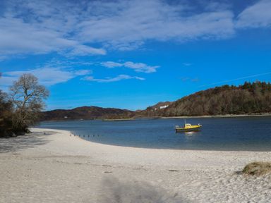 A sandy beach with a yellow boat on the water and hills in the background at Creag Mhor Lodge Back of Keppoch near Arisaig