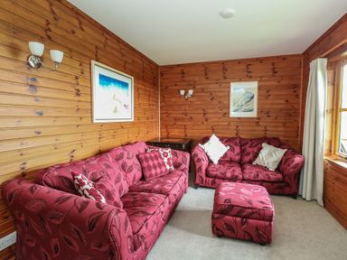 A living room with two red patterned sofas a matching ottoman wooden paneled walls and framed pictures at Creag Mhor Lodge Back of Keppoch near Arisaig