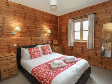 A bedroom with a double bed with white and red bedding two wooden bedside dressers wall lamps a window with curtains and a mirror on the wall at Creag Mhor Lodge Back of Keppoch near Arisaig