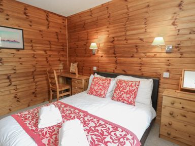 A bedroom with a double bed and wooden furniture including a desk chairs and a chest of drawers at Creag Mhor Lodge Back of Keppoch near Arisaig