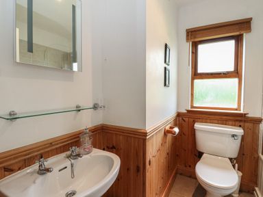 A bathroom with a white sink and mirror a toilet wooden paneling on walls and a window at Creag Mhor Lodge Back of Keppoch near Arisaig