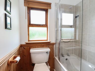 A bathroom with a toilet under a window and a bathtub with a shower at Creag Mhor Lodge Back of Keppoch near Arisaig