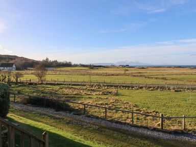 A rural landscape with fields fences a road and distant buildings at Glen Mhor Lodge in Arisaig