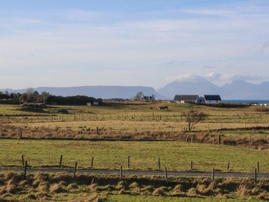 A rural landscape with fenced fields, houses, cows, a road, and mountains in the background at Glen Mhor Lodge in Arisaig