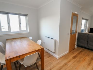 A dining area with a wooden table and white chairs next to windows and a room with a couch and a wooden door at Glen Mhor Lodge in Arisaig