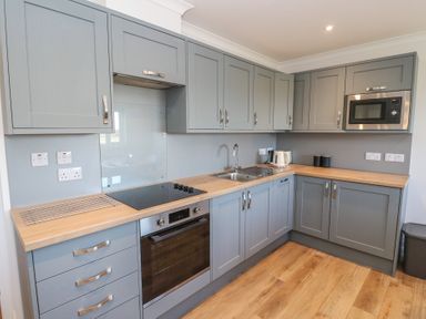 A kitchen with gray cabinets a built in oven a stovetop a microwave a sink a kettle and wooden countertops at Glen Mhor Lodge in Arisaig