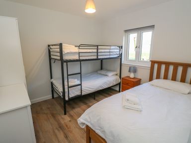 A bedroom with a bunk bed a double bed a wooden nightstand with a lamp and a window at Glen Mhor Lodge in Arisaig