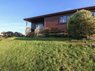 A wooden cabin with steps leading to a porch and a picnic table on grass at Glen Mhor Lodge in Arisaig