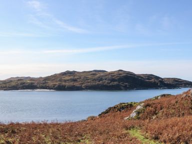 A body of water with an island covered in vegetation and hills in the background at Glen Mhor Lodge in Arisaig
