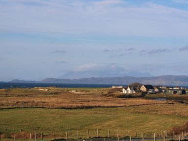 A rural landscape with fields fenced off and houses near the water at Glen Mhor Lodge in Arisaig