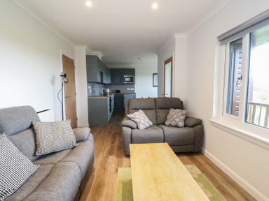 A living area with two grey sofas a wooden coffee table and a view into a kitchen with grey cabinets at Glen Mhor Lodge in Arisaig