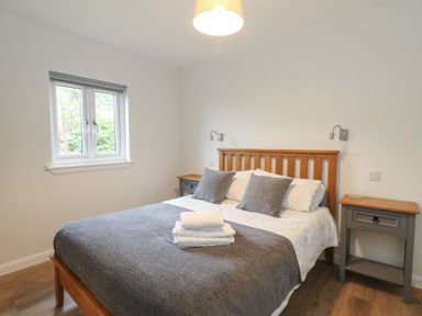 A bedroom with a wooden bed frame two grey pillows a grey bed cover two bedside tables and a window at Glen Mhor Lodge in Arisaig