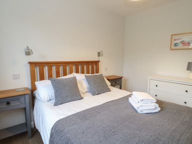 A bedroom with a bed with gray pillows and blanket two bedside tables and a white dresser at Glen Mhor Lodge in Arisaig