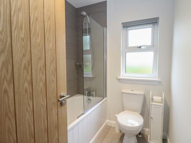 A bathroom with a bathtub and shower a toilet a window and a wooden door at Glen Mhor Lodge in Arisaig