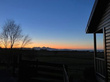 Sunset view with silhouetted trees and a building overlooking a landscape with distant mountains at Glen Mhor Lodge in Arisaig