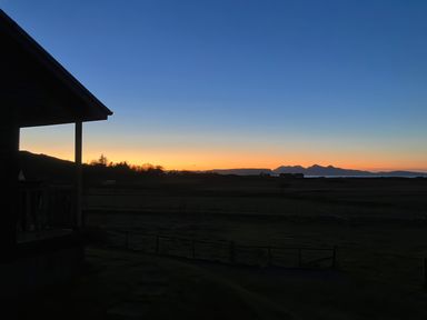 A view of a sunset over fields and distant hills with a house on the left side at Glen Mhor Lodge in Arisaig