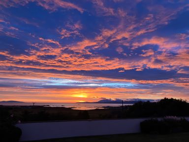 A view of a sunset over water with hills and a wall in the foreground at Glen Mhor Lodge Arisaig