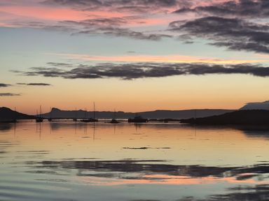 A calm body of water with boats anchored and mountains in the background at Glen Mhor Lodge in Arisaig