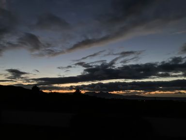 A landscape view of a sunset with dark clouds and silhouettes of trees and mountains at Glen Mhor Lodge in Arisaig
