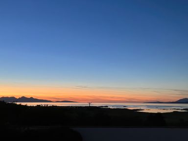 A coastal landscape at sunset with mountains and calm water at Glen Mhor Lodge in Arisaig