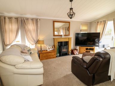A living room with a cream sofa brown armchair fireplace and a large television at The Lake House in Marston near Barkston
