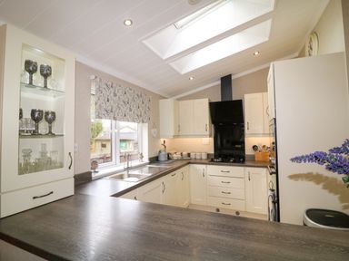 A kitchen with white cabinets a window with a floral blind and glassware displayed at The Lake House in Marston near Barkston