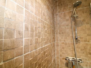 A shower area with beige tiled walls and a silver showerhead and control at The Lake House in Marston near Barkston