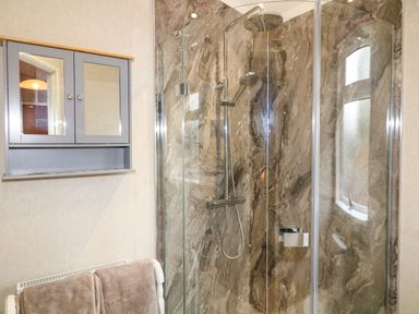 A bathroom with a glass shower enclosure a gray wall-mounted cabinet and towels on a radiator at The Lake House in Marston near Barkston