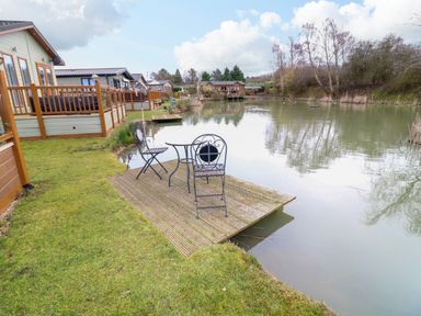 A lakeside view with chairs and a table on a wooden deck near homes at The Lake House in Marston near Barkston