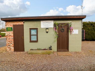 A small building with two brown doors and a window with flower decorations and signs on the wall at The Lake House in Marston near Barkston