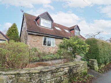 A stone house with a tiled roof and dormer windows surrounded by a garden and stone wall at Kerangarth in Corbridge