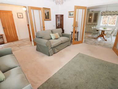 A living room with two sofas and a green rug opening into a dining area with a table and chairs at Kerangarth in Corbridge