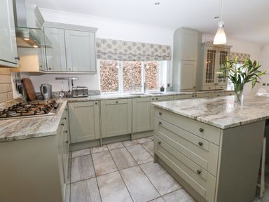 A kitchen with an island countertop a gas stove toaster kettle and flowers on the island at Kerangarth in Corbridge