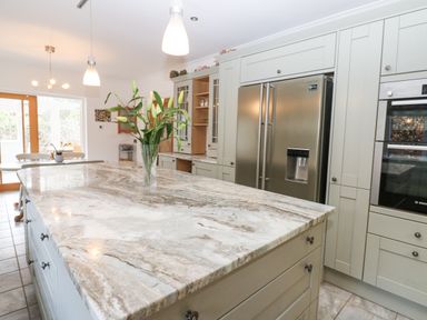 A kitchen with a large marble island countertop a vase with flowers pendant lights stainless steel refrigerator and built in oven at Kerangarth in Corbridge