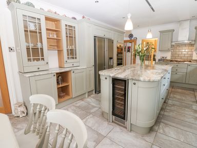 A kitchen with a central island, refrigerator, glass-front cabinets, and dining chairs at Kerangarth in Corbridge