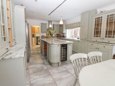 A kitchen with gray cabinets marble countertops an island with a vase and two pendant lights and a dining table with chairs at Kerangarth in Corbridge