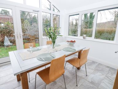 A dining area with a table set with placemats glasses and cutlery four wooden chairs and large windows at Kerangarth Corbridge