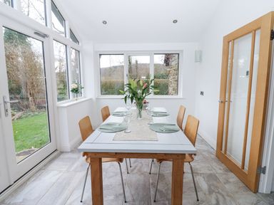A dining room with a rectangular table set for four by windows and a glass door at Kerangarth in Corbridge