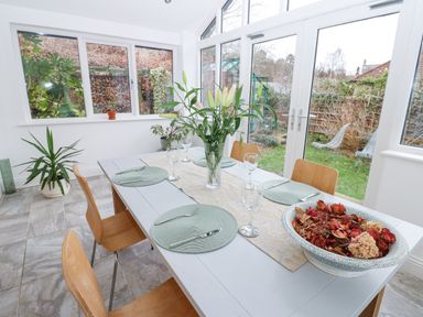 A dining area with a white table set with placemats glasses and cutlery and surrounded by wooden chairs next to large windows and glass doors showing a garden at Kerangarth in Corbridge