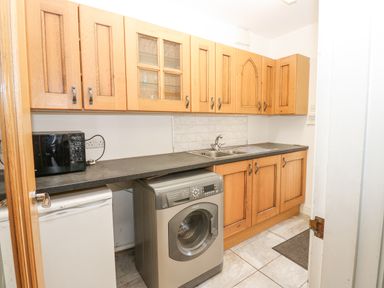 A laundry room with wooden cabinets a washing machine a microwave and a sink at Kerangarth in Corbridge