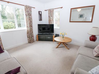 A living room with two sofas a round wooden table with flowers a television on a stand and floral curtains at Kerangarth in Corbridge