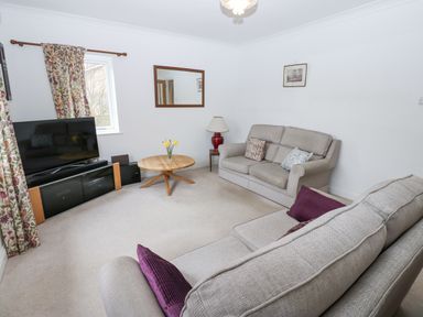 A living room with two sofas a round wooden coffee table a TV on a stand and floral curtains at Kerangarth in Corbridge