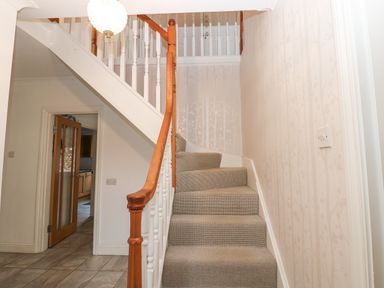 A carpeted staircase with wooden handrail and white spindles next to a hallway with tiled floor and wooden door at Kerangarth in Corbridge