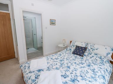 A bedroom with a double bed with floral bedding and a small round bedside table with a lamp at Kerangarth in Corbridge